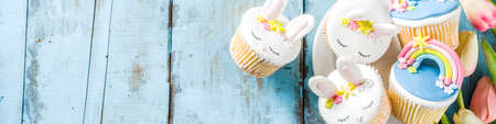 Easter holiday greeting card background. Cute homemade cupcakes with traditional Easter bunny, egg and springtime flowers decor. Happy easter concept. Copy space for your textの写真素材
