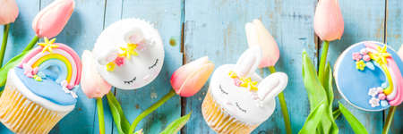 Easter holiday greeting card background. Cute homemade cupcakes with traditional Easter bunny, egg and springtime flowers decor. Happy easter concept. Copy space for your textの写真素材