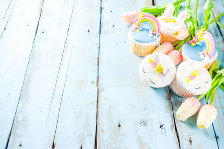 Easter holiday greeting card background. Cute homemade cupcakes with traditional Easter bunny, egg and springtime flowers decor. Happy easter concept. Copy space for your textの写真素材