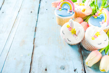 Easter holiday greeting card background. Cute homemade cupcakes with traditional Easter bunny, egg and springtime flowers decor. Happy easter concept. Copy space for your textの写真素材