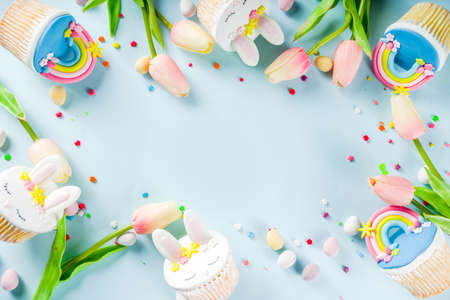 Easter holiday greeting card background. Cute homemade cupcakes with traditional Easter bunny, egg and springtime flowers decor. Happy easter concept. Copy space for your textの写真素材