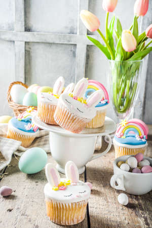 Easter holiday greeting card background. Cute homemade cupcakes with traditional Easter bunny, egg and springtime flowers decor. Happy easter concept. Copy space for your textの写真素材