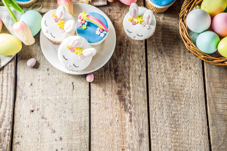 Easter holiday greeting card background. Cute homemade cupcakes with traditional Easter bunny, egg and springtime flowers decor. Happy easter concept. Copy space for your textの写真素材