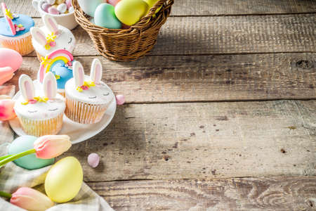 Easter holiday greeting card background. Cute homemade cupcakes with traditional Easter bunny, egg and springtime flowers decor. Happy easter concept. Copy space for your textの写真素材