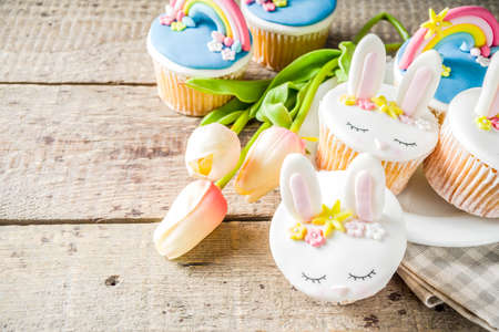Easter holiday greeting card background. Cute homemade cupcakes with traditional Easter bunny, egg and springtime flowers decor. Happy easter concept. Copy space for your textの写真素材