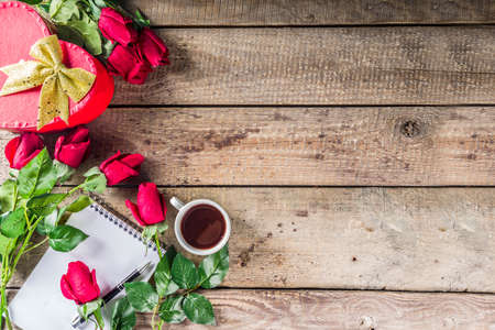 Valentine's day congratulations concept. Background for congratulation cards. Roses, valentine gift box with bow, cup of hot chocolate or coffee, notepad. On a wooden background, top view copy spaceの写真素材