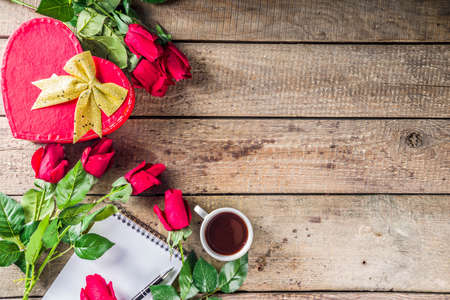 Valentine's day congratulations concept. Background for congratulation cards. Roses, valentine gift box with bow, cup of hot chocolate or coffee, notepad. On a wooden background, top view copy spaceの写真素材