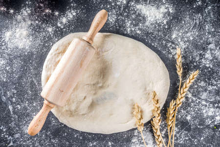 Baking background with dough. Cooking bread, pie cake baking background. Raw dough on black stone table with rolling pin top view copy spaceの写真素材