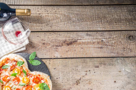 Pizza for Valentine day. Heart shaped homemade pizza margarita. Valentines day romantic menu concept. With wine bottle, roses flowers and and wineglass. Wooden background copy spaceの写真素材