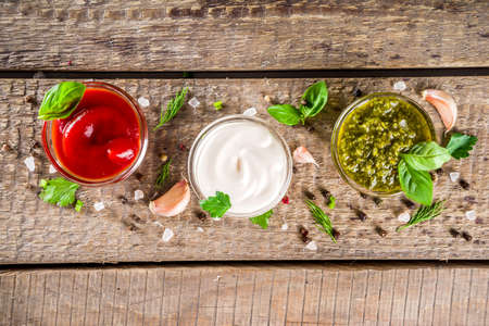 Set of sauces in small bowls - ketchup, mayonnaise, mustard, bbq sauce, pesto, classic burger sauce, with spices and herbs in. Wooden background copy space top viewの写真素材