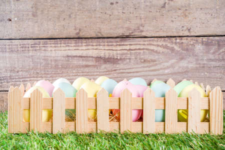 Colorful pastel Easter eggs on green and wooden garden terrace.  Funny spring decoration. Happy Easter greeting card background. の写真素材