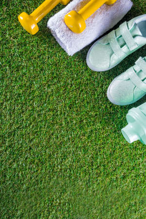 Summer sport, fitness, active lifestyle concept. Pastel sneakers, shaker for cocktail or water, towel, dumbbells. Fitness accessories for summer sport on green grass background flatlay copy spaceの写真素材