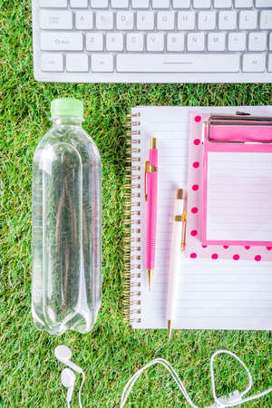 Summer office, work on vacation, freelance concept. Keyboard, notepad, earphones, office supplies, water and coffee on a green summer grass background. Flatlay top view copy space for your textの写真素材