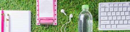 Summer office, work on vacation, freelance concept. Keyboard, notepad, earphones, office supplies, water and coffee on a green summer grass background. Flatlay top view copy space for your textの写真素材