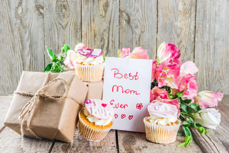 Happy moms day greeting background. Mothers day sweet cupcakes, with gift boxes, coffee cappuccino cup, flowers. Wooden background copy spaceの写真素材