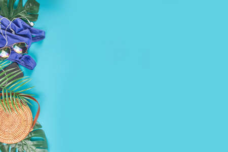 Summer vacation and travel concept. Beach accessories things - bag, hat, swimsuit, sunglasses, camera, tropical leaves on aquamarine, turquoise blue backdrop. Summer is coming trendy conceptの写真素材