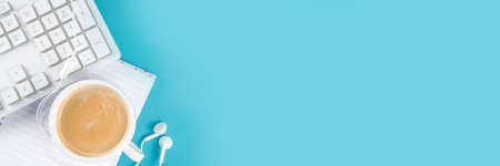 Office aquamarine, turquoise blue workplace backdrop with coffee cup, headphones and computer keyboard. Flat lay. Top view copy space for textの写真素材