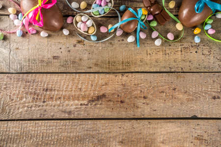 Easter card background. Chocolate Easter eggs and bunny rabbits with color ribbon and bows on wooden...