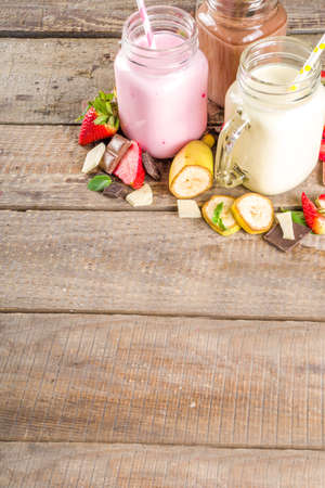 Three mason jars with milkshakes or smoothie. Summer healthy breakfast, lunch drinks - banana, chocolate and strawberry milkshakes on wooden backgroundの写真素材