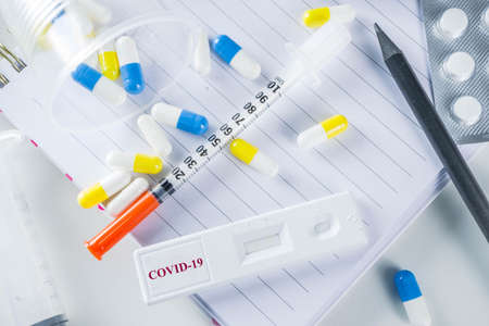 Worldwide coronavirus epidemic concept. Pandemic COVID-19, 2019-nCoV. Laboratory test strip for antibody or sars-cov-2 virus disease. In doctor hands. With pills, vaccination syringes, notebook.の写真素材