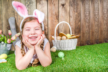 Cute little child girl with bunny ears on Easter holiday. With painted eggs basket, bunny toy and...