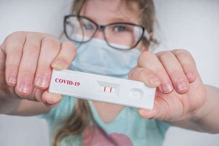 Worldwide coronavirus epidemic concept. Pandemic COVID-19, 2019-nCoV. Kid girl with positive test strip for antibody or sars-cov-2 virus disease in hands. White backgroundの写真素材