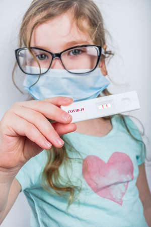 Worldwide coronavirus epidemic concept. Pandemic COVID-19, 2019-nCoV. Kid girl with positive test strip for antibody or sars-cov-2 virus disease in hands. White backgroundの写真素材