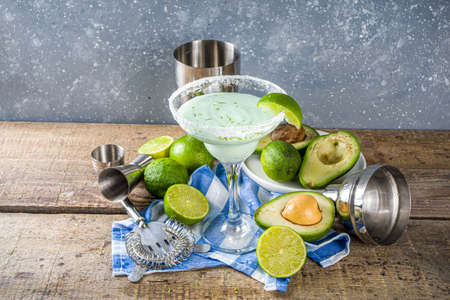 Alcoholic cocktail recipes and ideas. Avocado and lime margarita with salt, rustic wooden table copy...