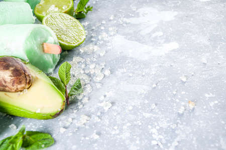 Homemade avocado ice creams. Vegan non-dairy ice cream. Avocado,lime and coconut healthy ice creams on grey stone background with fresh lime slices, avocados and ice.の写真素材