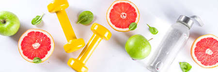 Fitness and healthy food lifestyle concept. Dumbbells, diet fruit and vegetable lunch box, water and jump rope on white background. Flatlay image, top view copy spaceの写真素材