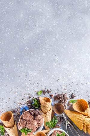 Homemade chocolate ice cream with chocolate pieces and shavings, and ice cream cones. In small white bowls on white grey stone table copy spaceの写真素材
