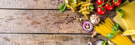 Assortment set of various raw pasta and condiments. Cooking italian pasta concept with fresh herbs and vegetables. Rustic style, wooden background top view copy spaceの写真素材