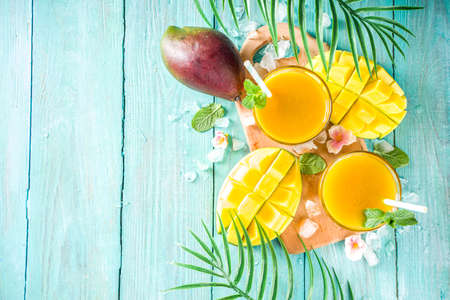 Fresh summer tropical fruit drink. Mango smoothie or mango juice, with fresh mango and tropical leaves on outdoor wooden background. Copy space top view.の写真素材