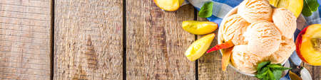 Homemade sweet peach ice cream. Peach gelato balls in small bowls, on wooden background with fresh peaches and mint leavesの写真素材