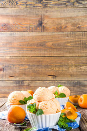 Homemade sweet apricot ice cream. Apricot gelato balls in small bowls, on wooden background with fresh apricots and mint leavesの写真素材