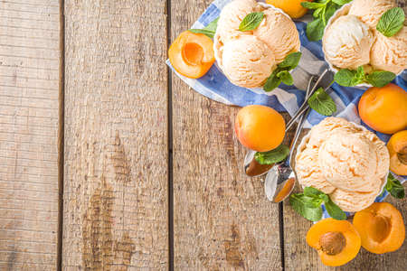 Homemade sweet apricot ice cream. Apricot gelato balls in small bowls, on wooden background with fresh apricots and mint leavesの写真素材