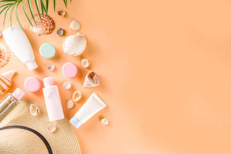 Summer cosmetics background. Summer skincare, sunscreen cosmetics, travel kit miniatures flat lay. Trendy peach background, with women bag, sea shells, tropical leaves, straw hat. Copy space above の写真素材