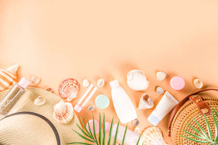 Summer cosmetics background. Summer skincare, sunscreen cosmetics, travel kit miniatures flat lay. Trendy peach background, with women bag, sea shells, tropical leaves, straw hat. Copy space above の写真素材