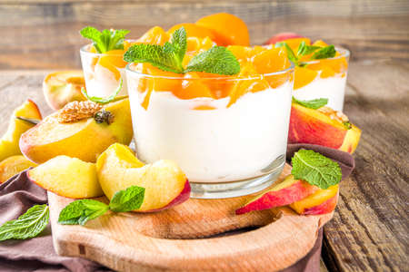 Curd or yogurt dessert with canned and fresh peaches, on wooden rustic background. Summer breakfast fruit dessert.の写真素材