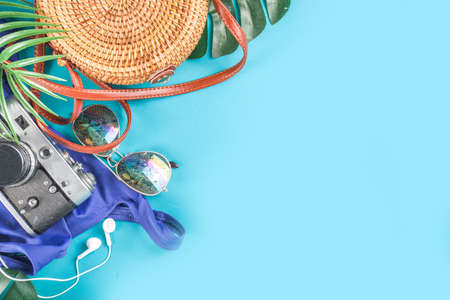 Summer vacation and travel concept. Beach accessories things - bag, hat, swimsuit, sunglasses, camera, tropical leaves on aquamarine, turquoise blue backdrop. Summer is coming trendy conceptの写真素材