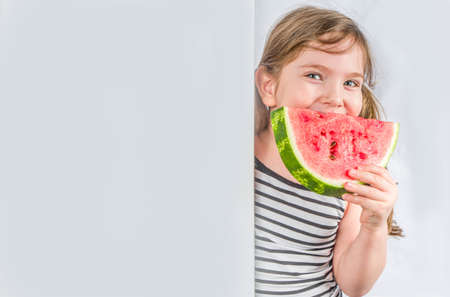 Happy little child with watermelon. Smiling kid girl eating watermelon slice, against white wall background, Copy spaceの写真素材