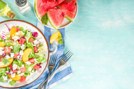 Summer diet salad with leaves of lettuce, watermelon, peach and feta cheese. On a light blue background copy spaceの写真素材