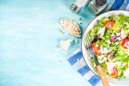 Vegan and vegetarian summer food background. Vegetable salad, with tomato, lettuce, cheese, fresh green lunch. Healthy eating concept. Light blue background copy spaceの写真素材