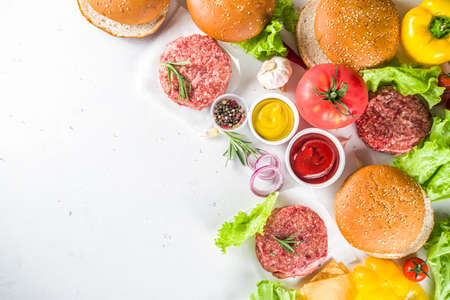 Cooking burger background. Set various cheeseburger  and beefburger ingredients - bun, tomatoes, onion, lettuce, sauces, cheese and raw burger cutlets, ready for barbecue grill. Burger bbq party fest concept, top view copy spaceの写真素材