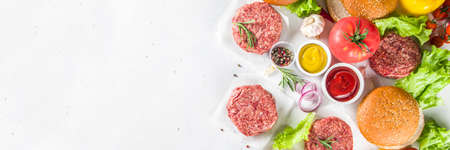 Cooking burger background. Set various cheeseburger  and beefburger ingredients - bun, tomatoes, onion, lettuce, sauces, cheese and raw burger cutlets, ready for barbecue grill. Burger bbq party fest concept, top view copy spaceの写真素材