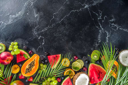 Assorted different summer tropical fresh raw fruits and berries. Clean eating, healthy lifestyle, diet and vitamin concept. Top view flat lay black table backgroundの写真素材