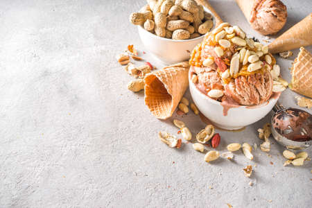Peanut butter ice cream. Sweet peanut ice cream with peanut butter topping and a lot of peanuts, on grey stone background with icecream waffle conesの写真素材