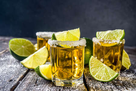 Golden tequila shots. Three tequila shot glasses with salt and lime slices, on wooden background copy spaceの写真素材