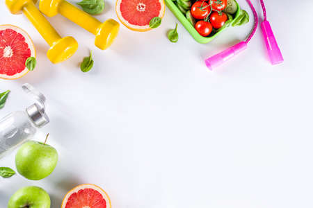 Fitness and healthy food lifestyle concept. Dumbbells, diet fruit and vegetable lunch box, water and jump rope on white background. Flatlay image, top view copy spaceの写真素材