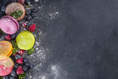 Colorful french macaron dessert. Set of various different tastes and color macaron cookies with berries, sugar powder and mint on dark grey stone backgroundの写真素材